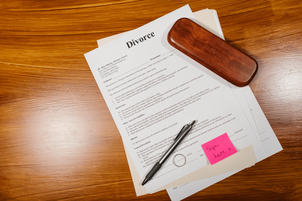 Divorce paperwork with a pen and a sticky note that reads "Sign here," symbolizing the process of legally acknowledging divorce papers.