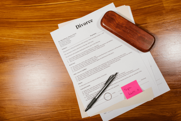 Divorce paperwork with a pen and a sticky note that reads "Sign here," symbolizing the process of legally acknowledging divorce papers.