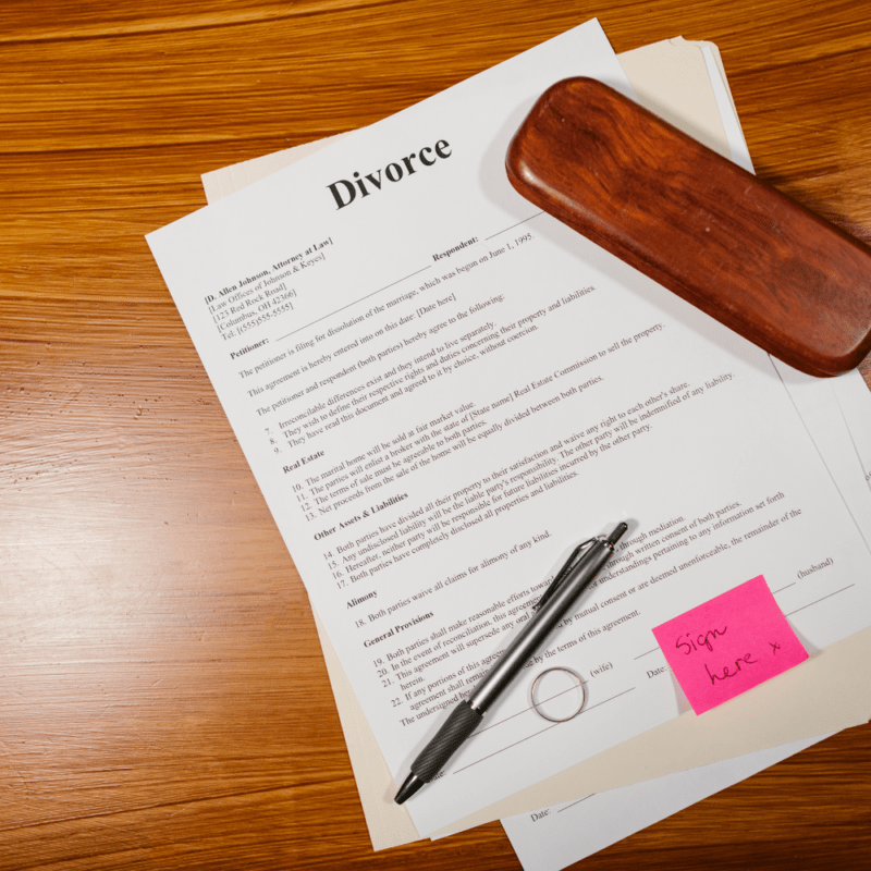 Divorce paperwork with a pen and a sticky note that reads "Sign here," symbolizing the process of legally acknowledging divorce papers.