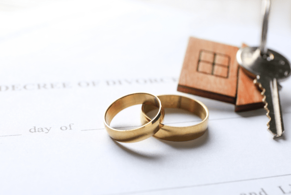 Two gold wedding rings on a divorce decree document with a wooden keychain and house key.