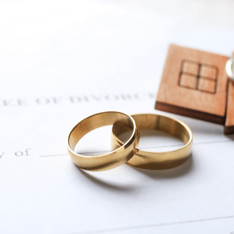 Two gold wedding rings on a divorce decree document with a wooden keychain and house key.