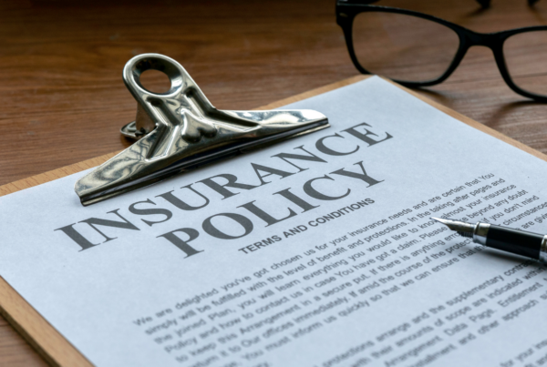 Close-up of a life insurance policy document on a clipboard, accompanied by a pen and glasses on a wooden desk.