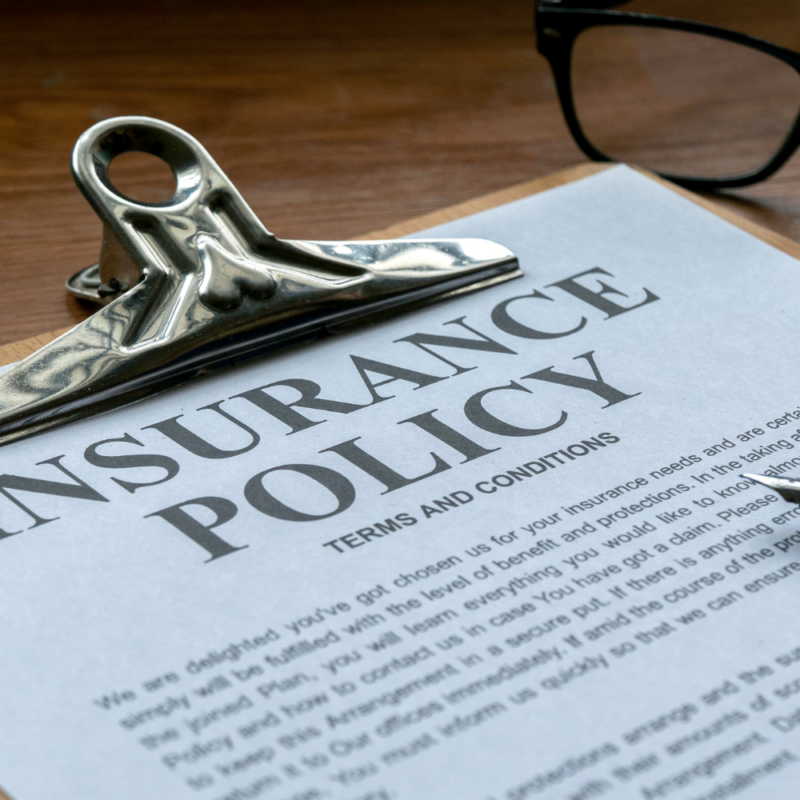 Close-up of a life insurance policy document on a clipboard, accompanied by a pen and glasses on a wooden desk.