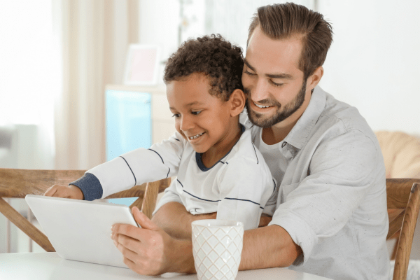 Man with boy on lap looking at a tablet and smiling