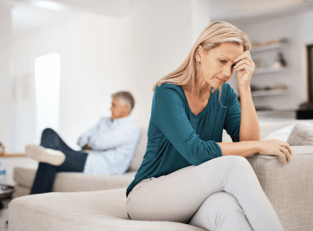 Leaving a toxic relationship. Woman at the edge of a sofa with her head in her hands with her spouse behind her on the other end of the sofa. It appears that he is not willing to listen.