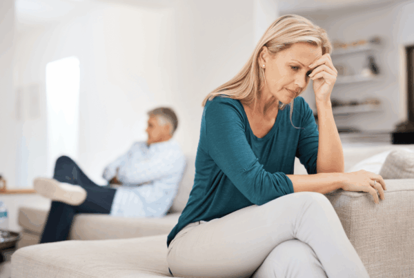Leaving a toxic relationship. Woman at the edge of a sofa with her head in her hands with her spouse behind her on the other end of the sofa. It appears that he is not willing to listen.